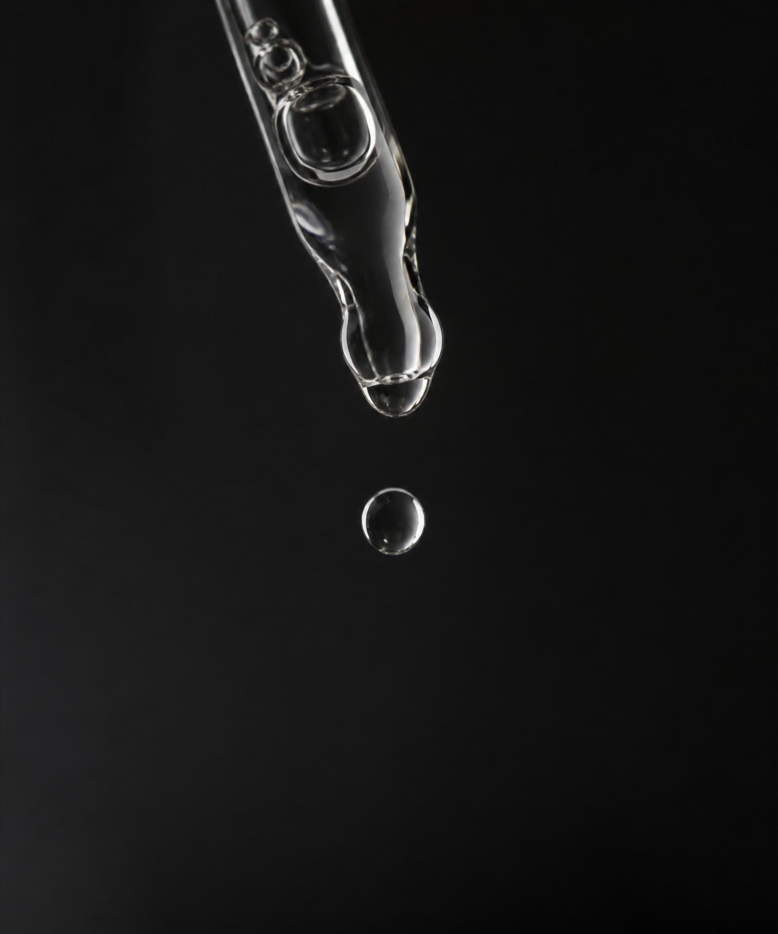 Macro de gota de sérum caindo do conta-gotas — silêncio editorial